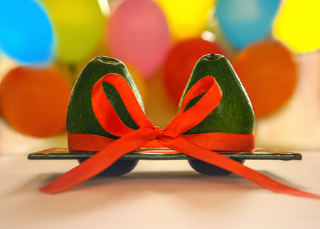 Green avocado with red silk ribbon on colorful balloons background. Healthy care and relationship symbol. Minimal style romance love creative concept Valentines day, wedding betrothal anniversaryの写真素材