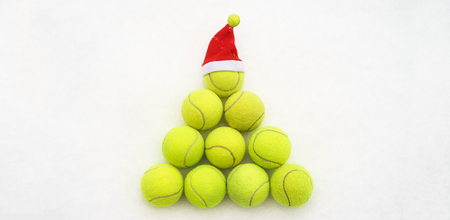 Santa hat on tennis ball on white snow background. Merry Christmas and New year concept with tennis balls. Yellow green color tennis balls in shape fir tree. Close up, sport lifestyle. Isolated, horizontalの写真素材