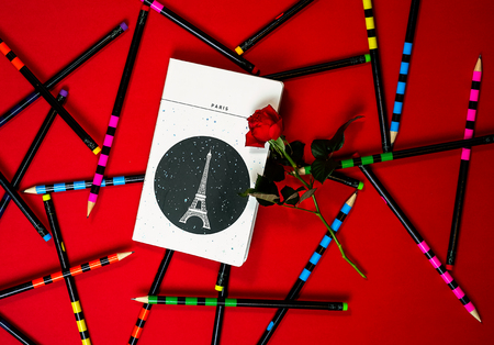 Flat lay layout white notebook Paris and red rose on red  with colorful office pencils.の写真素材