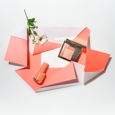 Creative layout made of flower, blusher palette and nail polish on folded paper of living coral color on whiteの写真素材