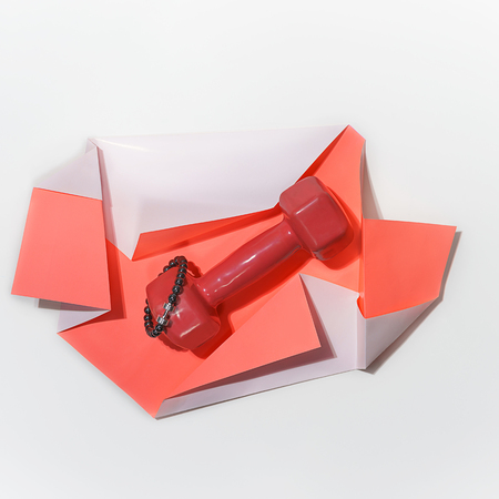 Concept for gift with female bracelet with silver dumbbell and red dumbbell on folded paper of pastel coral color on whiteの写真素材