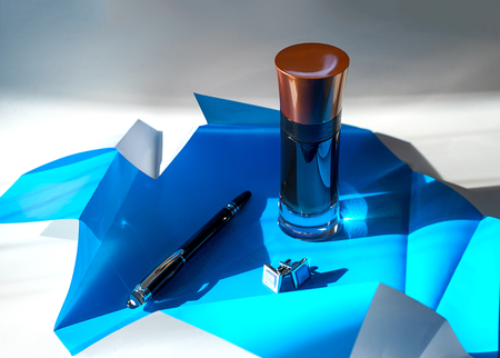 Creative layout made of mens perfume, black pen and cuffinks on folded paper of blue color.の写真素材