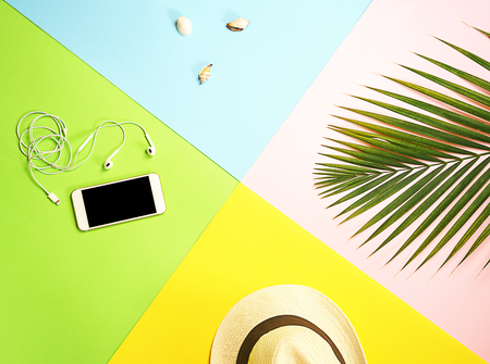 Flat lay traveler accessories layout: tropical palm leaf, white straw hat, mobile phone and headphones, seashells on colorful background. Travel vacation summer concept. top view composition.の写真素材