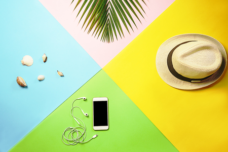 Flat lay traveler accessories layout: tropical palm leaf, white straw hat, mobile phone and headphones, seashells on colorful background. Travel vacation summer concept. top view composition.の写真素材