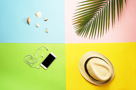 Flat lay traveler accessories layout: tropical palm leaf, white straw hat, mobile phone and headphones, seashells on colorful background. Travel vacation summer concept. top view composition.の写真素材