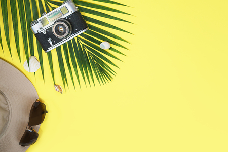 Flat lay with traveler accessories: tropical palm leaf, retro camera, sun hat, fashion sunglasses and seashells on yellow background, with space for text. Travel, summer concept. Top view.の写真素材