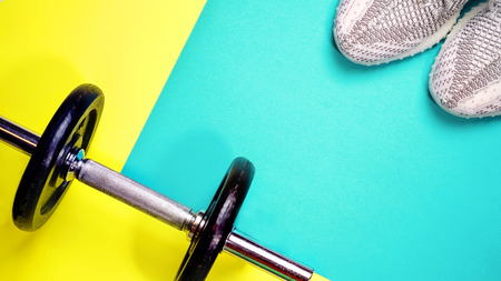 Fitness equipment on yellow and blue color background. Healthy and active lifestyle concept with trendy sneakers, dumbbell. Copy space, flat lay, top viewの写真素材