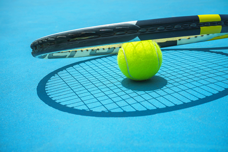 Summer sport concept with tennis ball and racket on blue hard tennis court. Top view, copy space. Blue and yellow.の写真素材