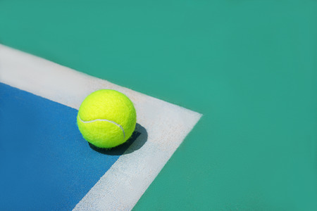 Summer sport concept with tennis ball on white line on hard tennis court. Flat lay, top view, copy space. Blue and green.の写真素材
