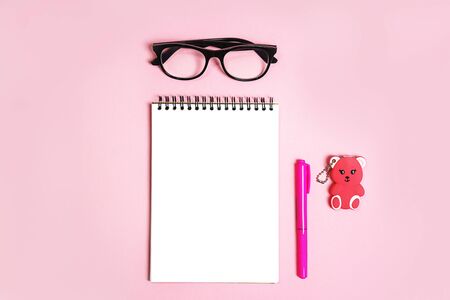 Notepad with trendy glasses and pink coral pen and toy bear gift on pastel pink background. Study, office layout. Flat lay, top view, copy space. Back to school, business minimal concept. Close up.の写真素材
