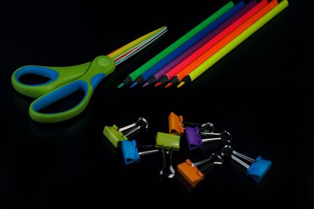 Back to school background with pencils, scissors, colorful paper clips on black backdrop. Flat lay, top view, copy space.の写真素材