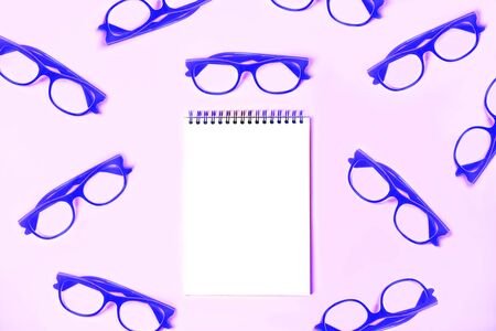 Notepad with trendy blue glasses on pastel pink violet background. Study, office layout. Flat lay, top view, copy space. Back to school, business concept.の写真素材