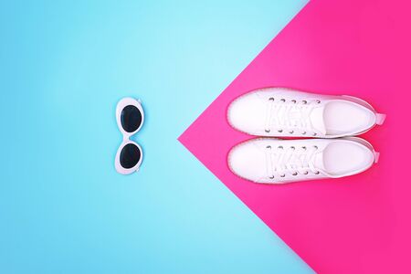 White sneakers and white sunglasses are lying on bright neon color blue pink background. Top view. Flat lay. Copy space.の写真素材