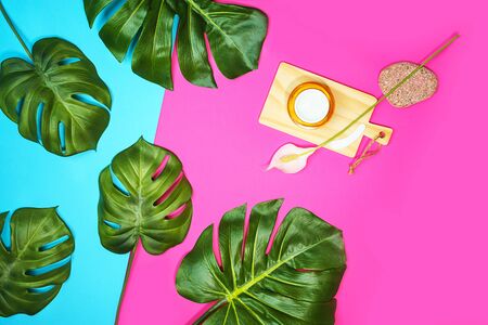 Tropical leaves Monstera isolated, Swiss Cheese Plant and jar of cream or mask for beautiful skin or cosmetics serum, flower on pink blue background. Facial treatment concept beauty. Flat lay.の写真素材