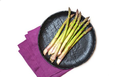 Fresh green asparagus on black ceramic dish and pink linen napkin on white background, isolated. Close up, flat lay, top view. Diet, healthy lifestyle concept.の写真素材
