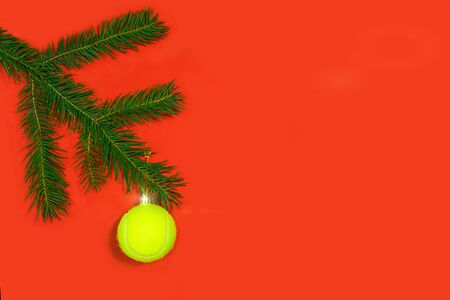 Tennis Christmas, Happy New Year concept with tennis ball as Christmas tree toy decoration and fir tree branches on redの写真素材