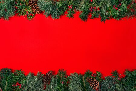 Christmas frame made of fir branches with berries on redの写真素材