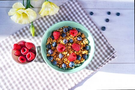 Bowl of homemade granola with fresh berries on gray wooden background. Top view, flat lay. Trendy mint green blue color of bowl and shadows on the table.の写真素材