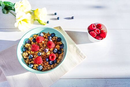 Bowl of homemade granola with fresh berries on gray wooden background. Top view, flat lay. Trendy mint green blue color of bowl and shadows on the table.の写真素材