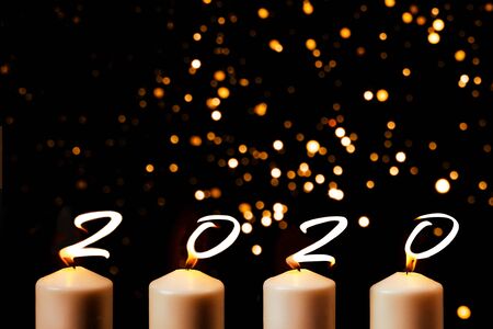 Happy New Year 2020 is written with candle flames on blurred gold black background. Concept of greeting card, holiday party celebration. Top view, flat lay, copy space.の写真素材