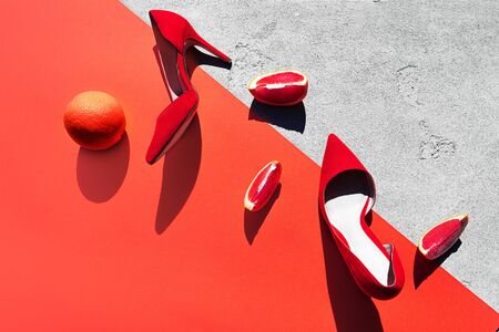 Red high heel shoes with grapefruit on pink coral color and concrete background. Fashion outfit abstract art layout. Top view, flat lay, copy space. Valentine's day modern concept.の写真素材