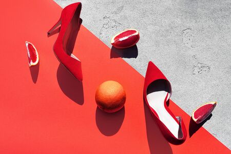 Red high heel shoes with grapefruit on pink coral color and concrete background. Fashion outfit abstract art layout. Top view, flat lay, copy space. Valentine's day modern concept.の写真素材
