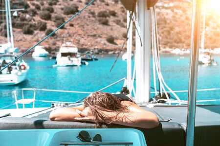 Young happy woman feels fun on the luxury sail boat yacht catamaran in turquoise sea in summer holidays. Caucasian female model. Blue white striped dress, sunglasses, on a background of yacht.の写真素材