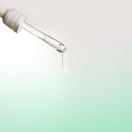 Pipette with drop of serum or hyaluronic acid on gray green natural color background. Beauty cosmetic consept for hydrating face masks, skin care solutions. Selective focus.の写真素材