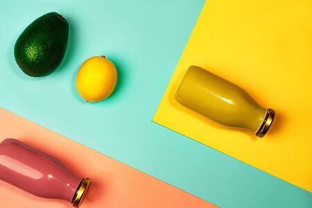 Bottles of multicolored juices or smoothies, lemon and avocado on yellow, pink coral and trendy mint green blue background. Flat lay, top view, close up. Minimal style.の写真素材