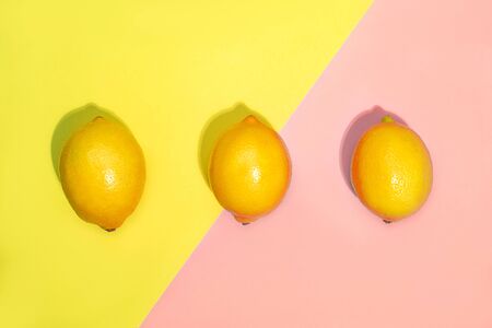 Creative pattern made of lemons on bright yellow and pastel pink background. Fruit minimal concept. Top view, flat lay, close up.の写真素材