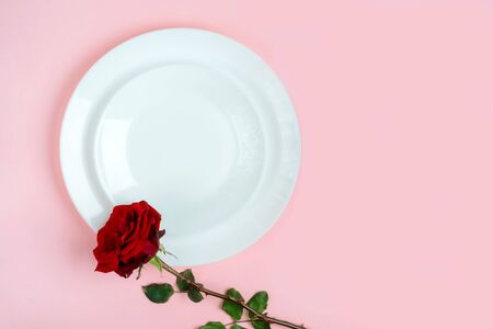 Romantic table setting for Valentines day or dinner date celebration wedding. Valentines day concept with red rose bud white plates on pastel pink tablecloth background. Flat lay, top view copy space.の写真素材