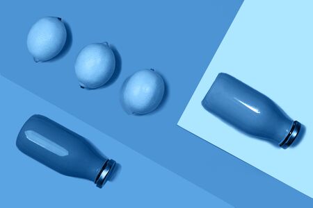Bottles of multicolored juices or smoothies and lemon on trendy classic blue background. Flat lay, top view, close up. Minimal style. Classic Blue color of the Year 2020 inscription.の写真素材