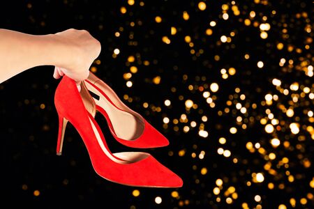 Woman holds fashionable red shoes in her hand on defocused abstract Christmas party background. Valentine's day, New Year party greeting card concept.の写真素材