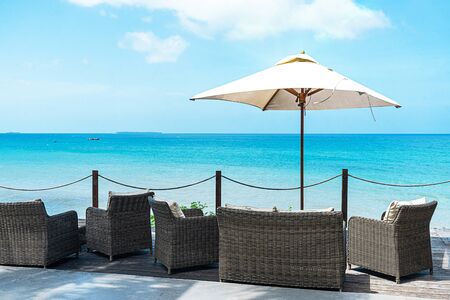 An outdoor cafe with wicker furniture and sun umbrellas on turquoise sea background. Tropical holidays concept.の写真素材