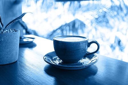Color 2020 classic blue. Cup of coffee on tropical background, colored in blue.の写真素材