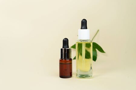 Various glass bottles with herbal CBD oil, THC tincture and hemp leaf on pastel beige background. Flat lay, minimal style. Cosmetics CBD oil. Essential natural oils for face and body.の写真素材