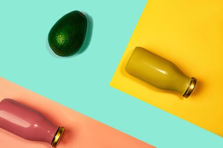 Bottles of multicolored juices or smoothies and avocado on yellow, pink coral and trendy mint green blue background. Flat lay, top view, close up. Minimal style.の写真素材