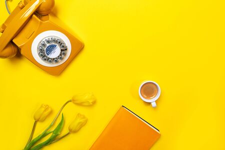 Yellow layout with retro rotary telephone, cup of coffee, flowers and notebook. Flat lay, top view, copy space.の写真素材