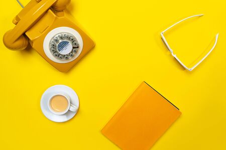 Yellow layout with retro rotary telephone, cup of coffee, sunglasses and notebook. Flat lay, top view, copy space.の写真素材