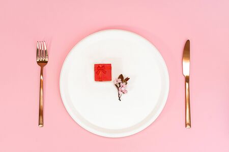 Spring cherry flower and red gift box on top of cream color plate, knife and fork. On a pink background. Flat lay, copy space. Cherry blossom.の写真素材