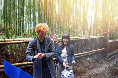 Kyoto, Japan - 03.17.20 Happy young beautiful Japanese couple take a selfie in bamboo forest. The bamboo groves of Arashiyama, Kyoto, Japan. Arashiyama is a district on the western outskirts of Kyoto.のeditorial素材
