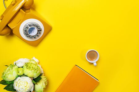 Yellow layout with retro rotary telephone, cup of coffee, flowers and notebook. Flat lay, top view, copy space.の写真素材