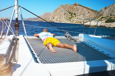 Happy young man feels happy on the luxury sail boat yacht catamaran in turquoise sea in summer holidays on island. Caucasian male model.の写真素材