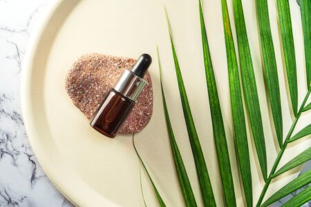 Herbal CBD oil bottle aroma dropper on glass and palm leaf on pastel beige plate and marble background. THC tincture. Minimal style. Cosmetics CBD oil. Essential natural oils for face and body.の写真素材