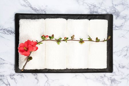 Beauty and spa concept. White towels and red flower on black tray on marble background. Flat lay. Japanese relaxation style.の写真素材