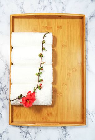 Beauty and spa concept. White towels and red flower on bamboo tray on marble background. Flat lay.の写真素材