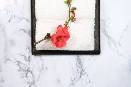 Beauty and spa concept. White towels and red flower on black tray on marble background. Flat lay. Japanese relaxation style.の写真素材