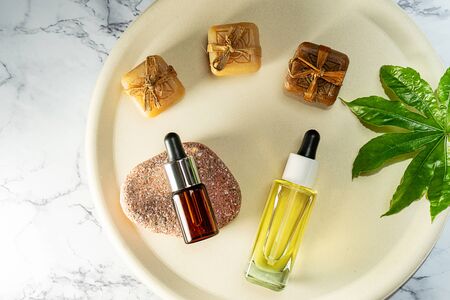 Herbal CBD oil bottles aroma dropper on glass and hemp leaf on pastel beige plate and marble background. THC tincture. Minimal style. Cosmetics CBD oil. Essential natural oils for face and body.の写真素材