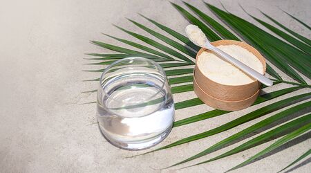 Closeup collagen with a spoon and glass of water on concrete background. Trendy healthy and beauty concept.の写真素材