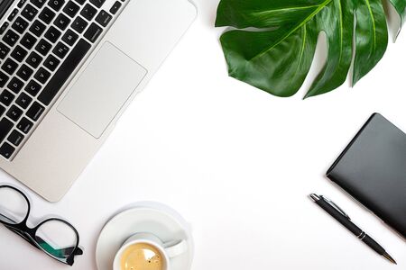 Top view of white office desk with laptop, notebook, palm leaf, cup of coffee and supplies. Working from home concept. Top view with copy space. Close up.の写真素材